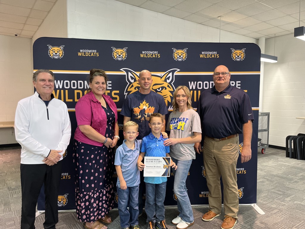 From left to right: Superintendent Mr. Mock, Elementary Principal Mrs. Lafontaine, Braxton and family, Board President Mr. Miller. They're all standing in front of the Woodmore Wildcats backdrop in the high school media center.