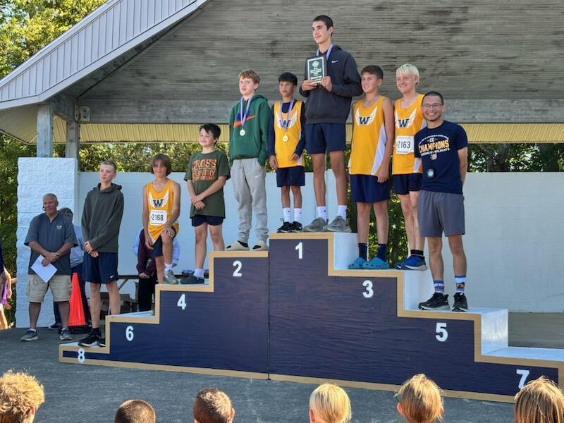 Boys Cross Country Team stands on the podium with Mr. Kigar