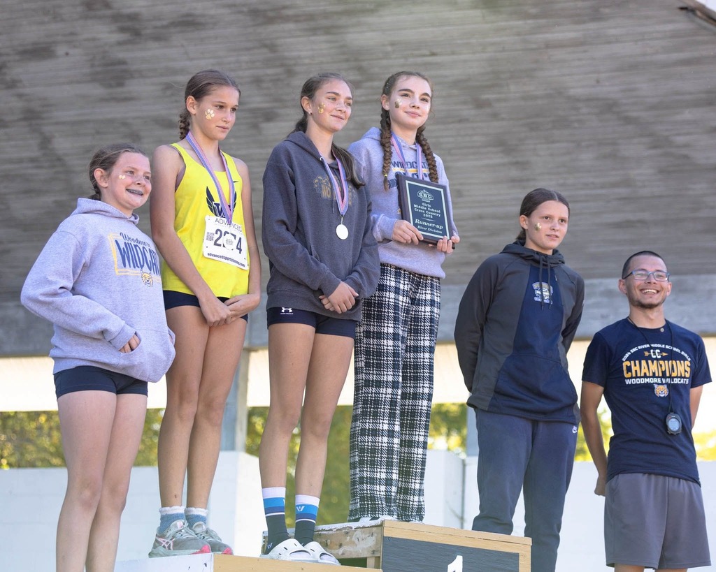 Girls MS Cross Country team stands on the podium with Mr. Kigar