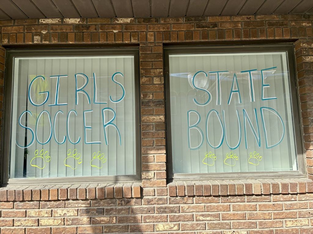 The Board Office has windows decorated to celebrate. This one says "GIRLS SOCCER STATE BOUND" with two paw prints.