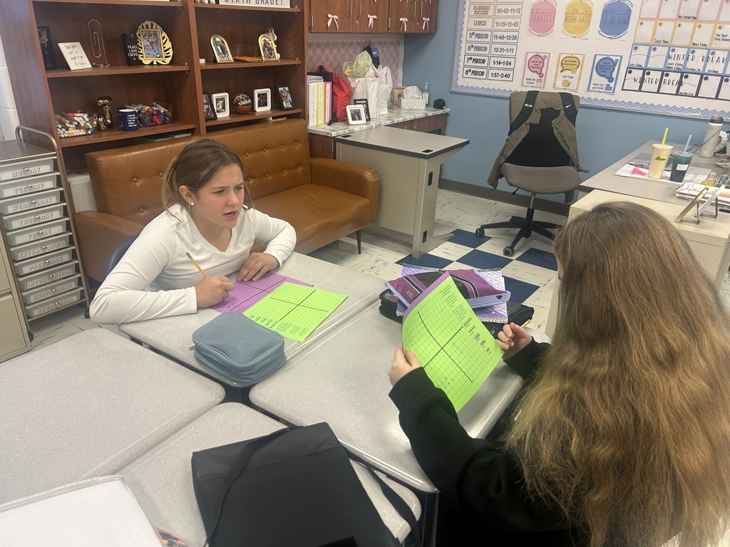 Two students are playing Coordinate Grid Battleship while sitting across from each other at their desks.