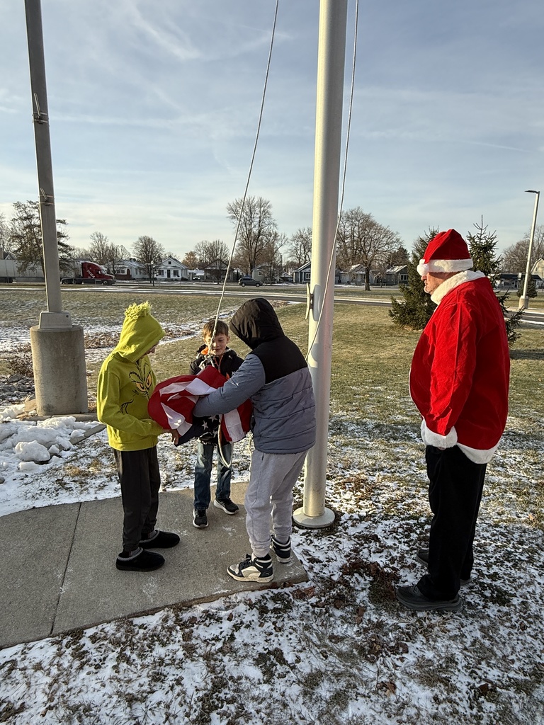 Our three students unfold the flag to get it attached to the rope pulley in order to raise it up the flag pole - overseen by Mr. Barrett in a Santa constume.