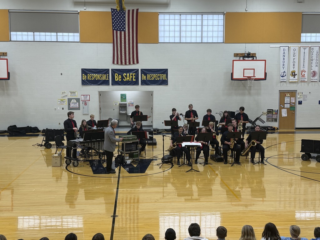 Our jazz band performs in the elementary/middle school gym. They are dressed in all black with red neck ties. Mr. Emerine, our band conductor, stands in front.