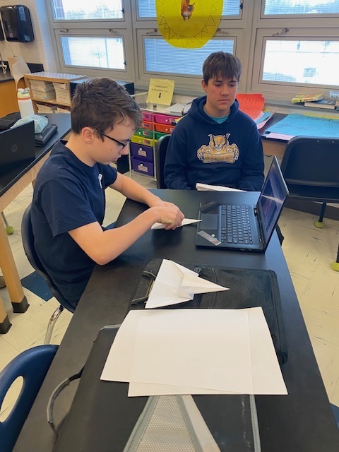 Two seventh grade students are back at their desk making revisions to their paper airplanes.