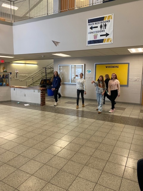 7th grade students test their paper airplanes in the cafetorium to see how far they can go! (Students are standing and throwing their paper airplanes)