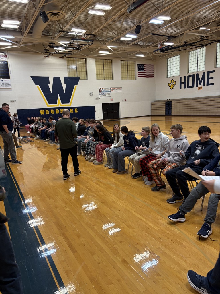 Students are sitting on chairs, lined up in the gym, with multiple teachers keeping an eye on the game!