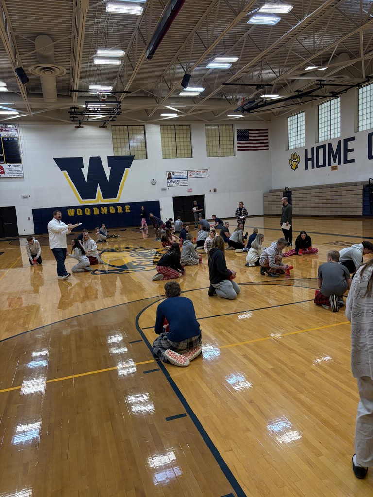 Students are sitting on the floor with cups, listening to instructions from Mr. Huss.