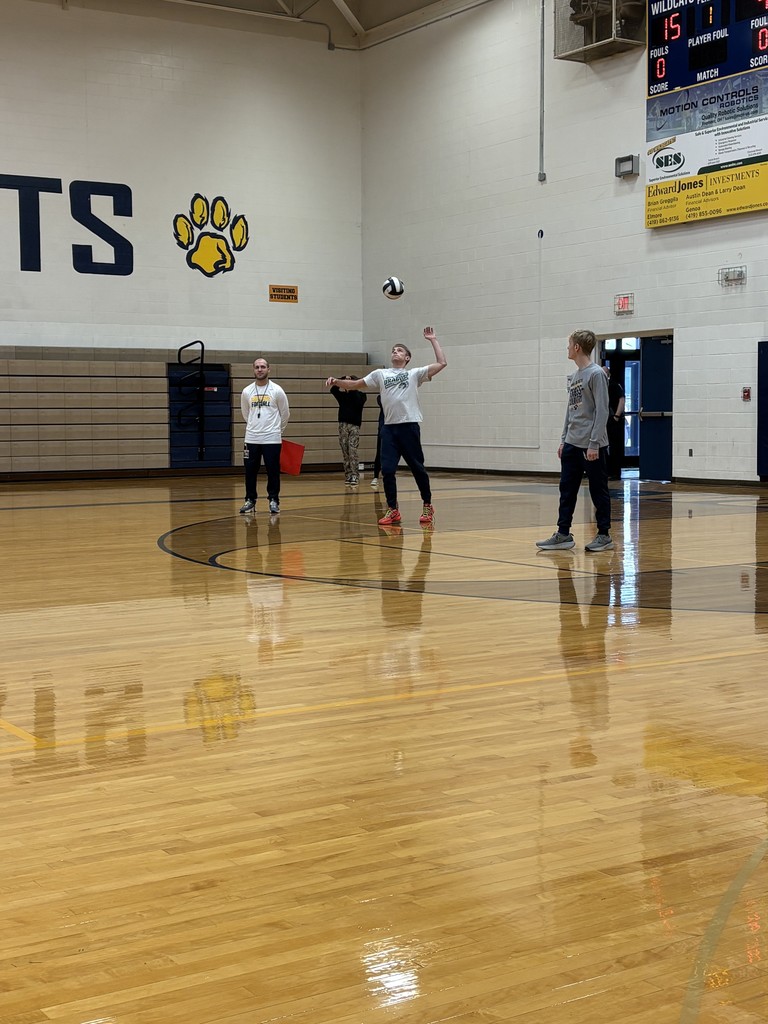 A student is mid serve. Mr. Unverferth is in the background as a line ref.