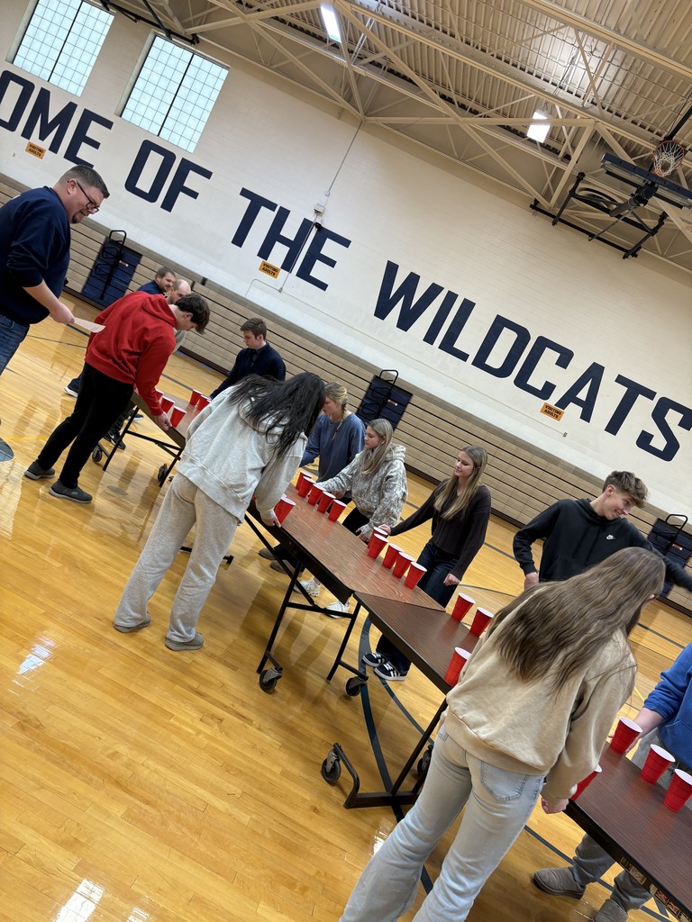 Students are lined up on either side of folding tables in the gym flipping cups as one of their games.