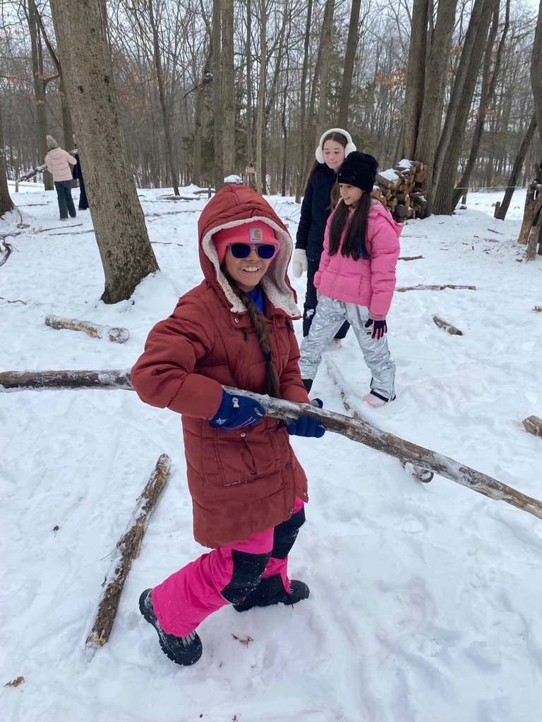 A sixth grade student carries a large stick with two other students watching in the background. This was part of their outdoor activities and team building exercises.