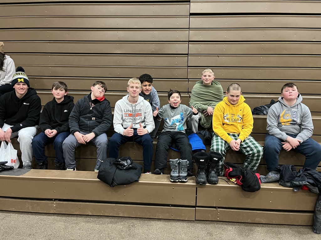 A group of sixth grade boys (and one high school cabin leader) sit on the bleachers inside after arriving to camp.