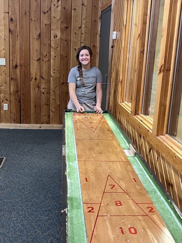 A sixth grade student stands at the end of the shuffleboard table and poses for the picture while playing a game.
