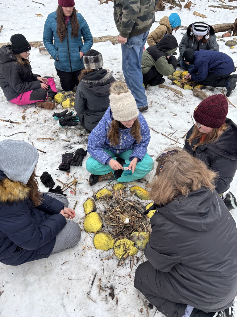 Multiple groups of students are gathered around the different small fires that they all built as part of a class at camp.