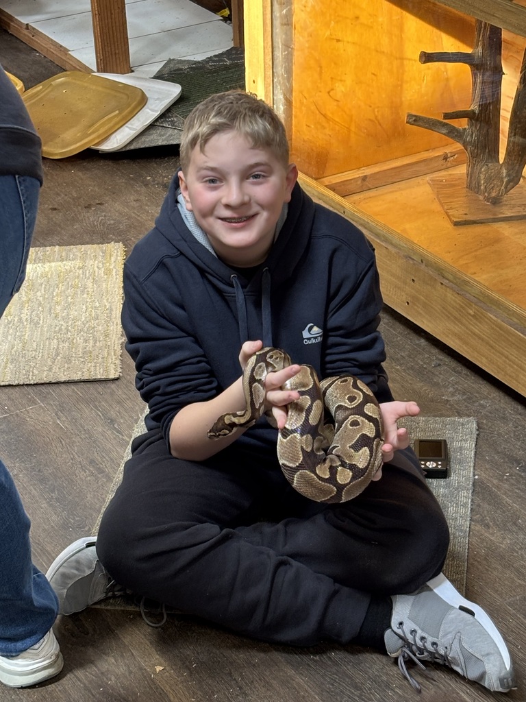 A student smiles while sitting on the floor holding a snake.