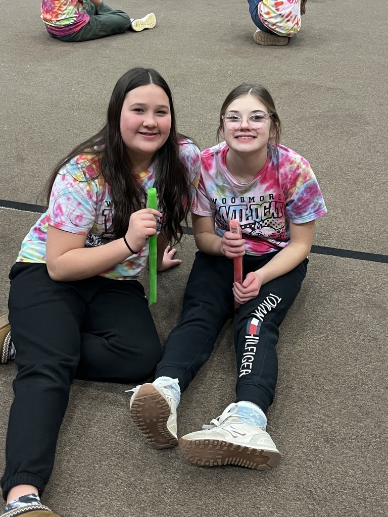 Two students sit in their tie dyed shirts in the gym eating popsicles.