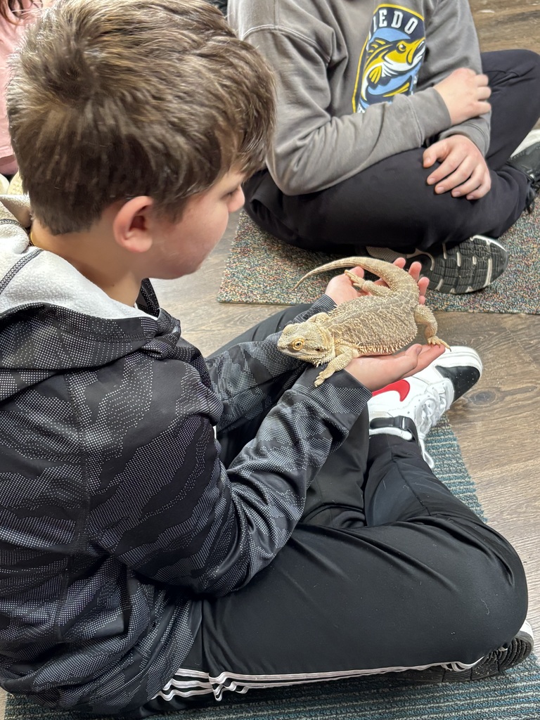 A sixth grade student holds a bearded dragon in his hands while sitting on the floor.