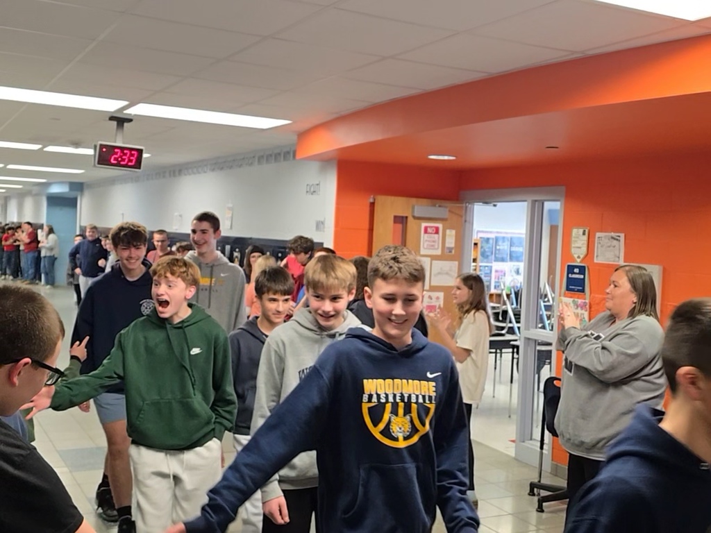 Boys 8th grade basketball team walks down the hallway lined with students and teachers who are clapping. The athletes give high fives as they walk past.