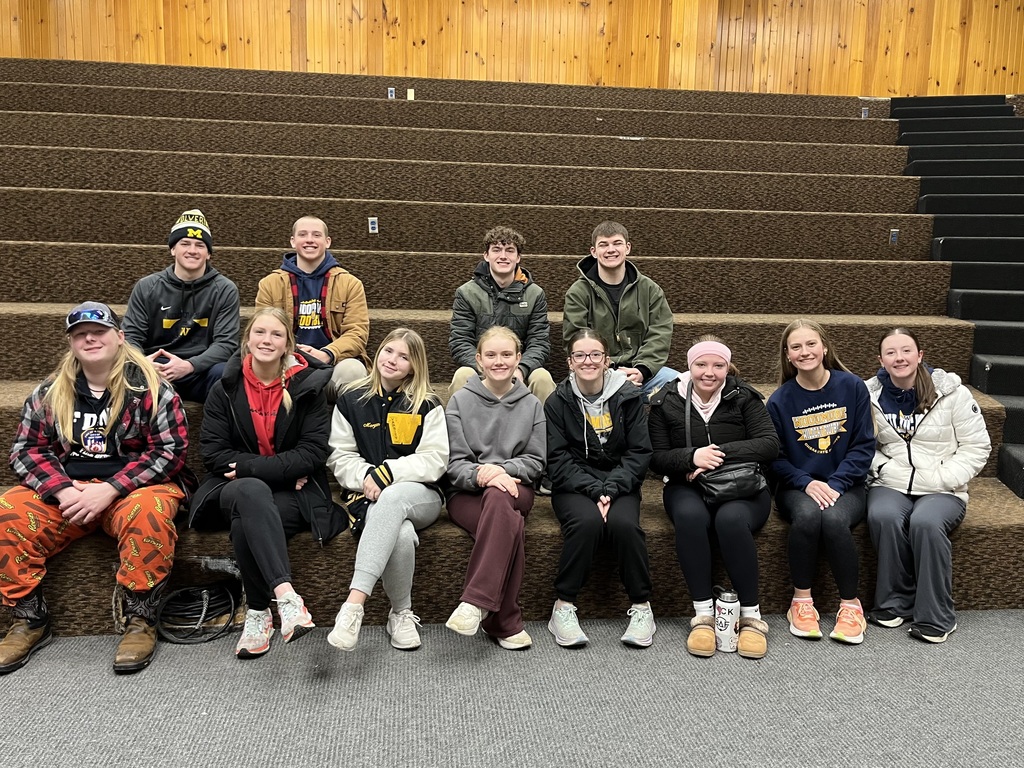 Twelve high school students sit on steps, posing for a picture. All are looking at the camera and smiling.