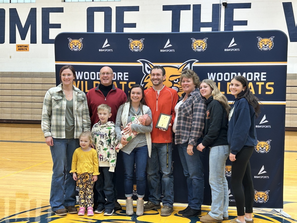Mr. Avers stands with his family and the students who nominated him in the gym in front of the Woodmore backdrop.