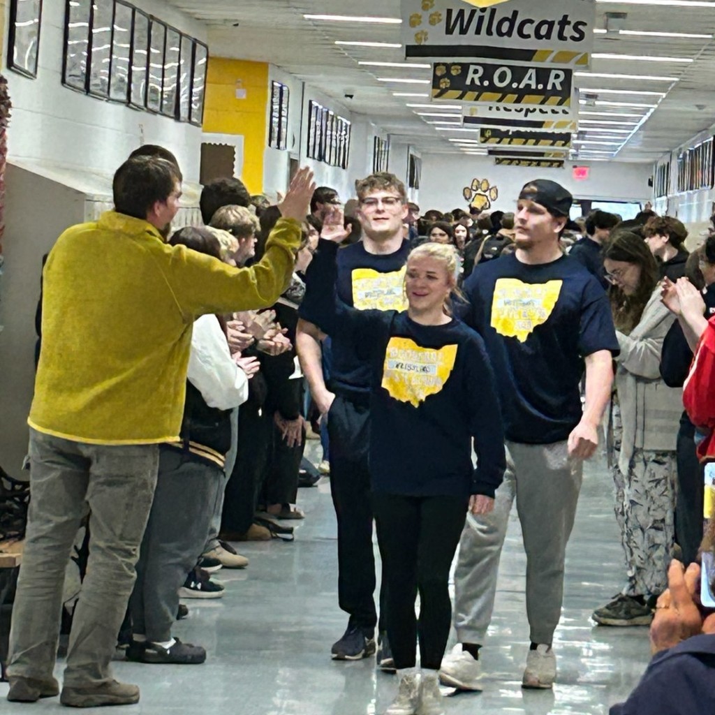 Three wrestlers walk down the hallway, lined by students and staff. Mr. Miller high fives the front wrestler.
