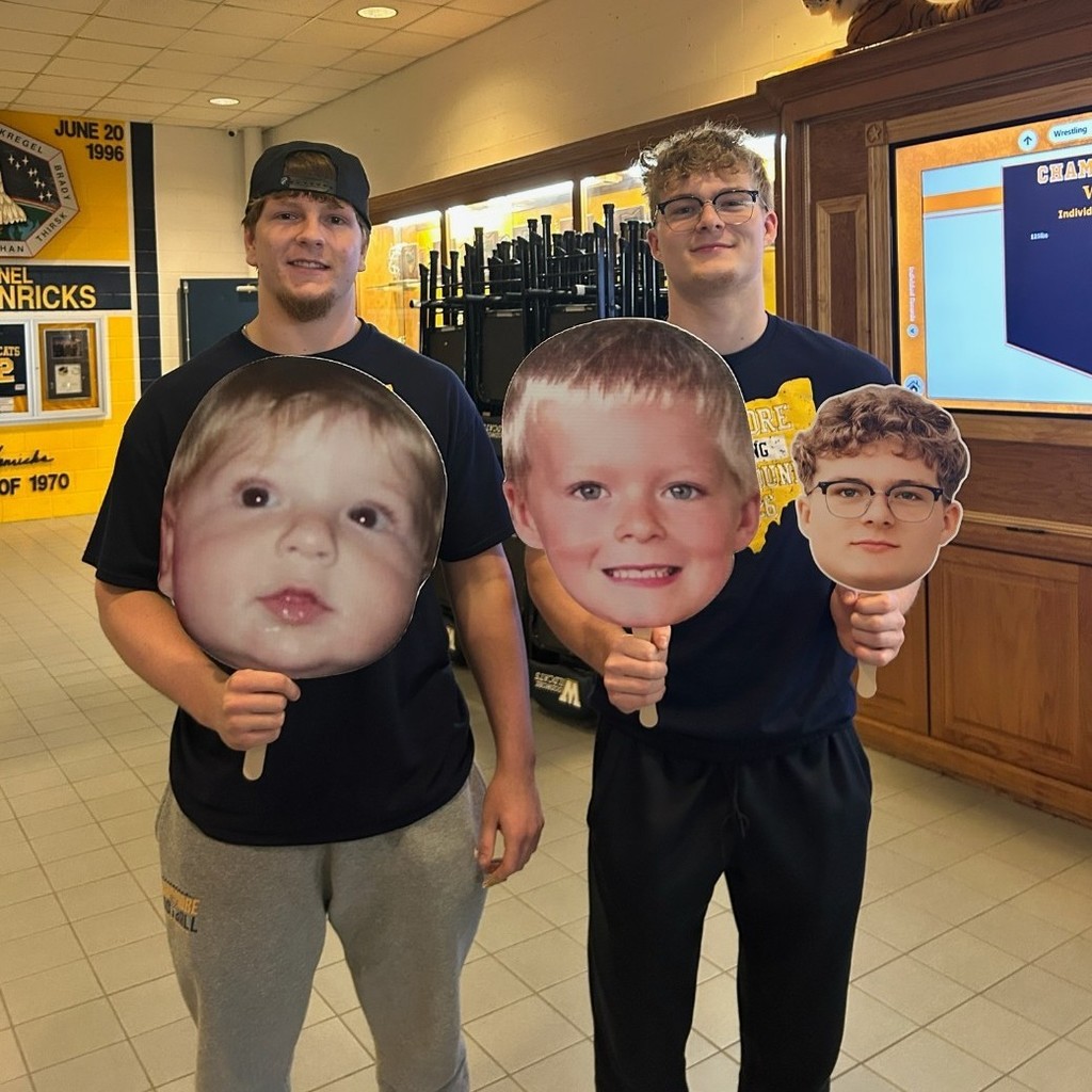 Two wrestlers hold up giant heads of themselves as small children while standing in the main hall. 