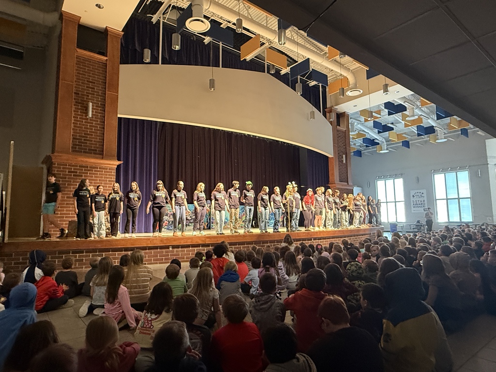 The cast of The Little Mermaid stands at the front of the stage with elementary and middle school students sitting on the floor watching the performance.