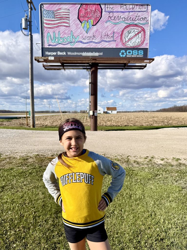 Harper posing in front of her actual billboard on St. Rt. 51. It is a sunny day and the billboard is above her in the picture.