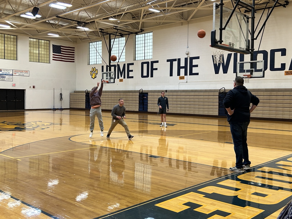 Carson Slates and Mr. Black are on the court shooting basketballs toward the same hoop. Mr. Fannin and another student look on. 