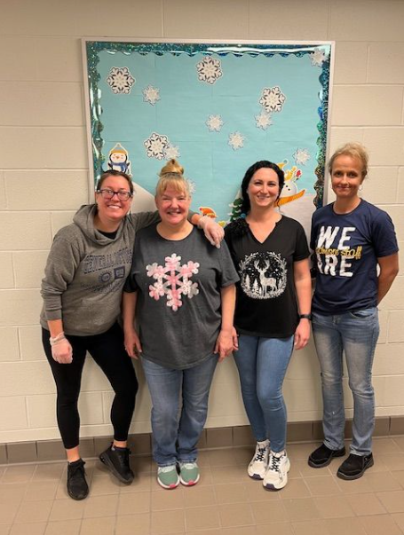 The Prekindergarten through 8th grade lunch heroes stand against a wall with a bulletin board behind them to pose for a picture. 