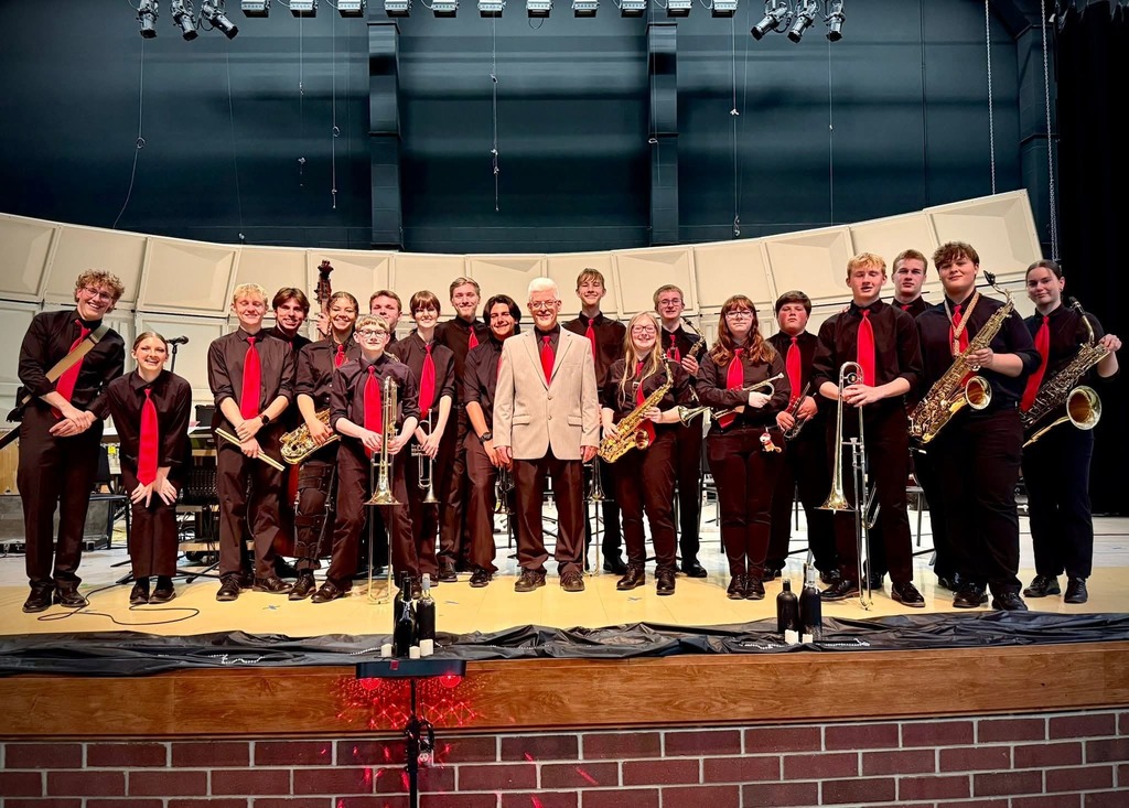 The jazz band and Mr. Emerine pose for a picture at the front of the stage in the elementary school.