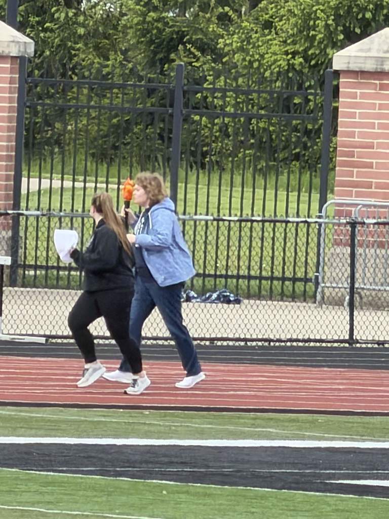 Evie running on the track, carrying the torch and being guided by another student.