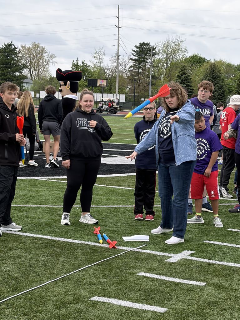 Students participating in a foam lawn dart event on the field at Perkins High School. There are students in black from Perkins helping out with the event.