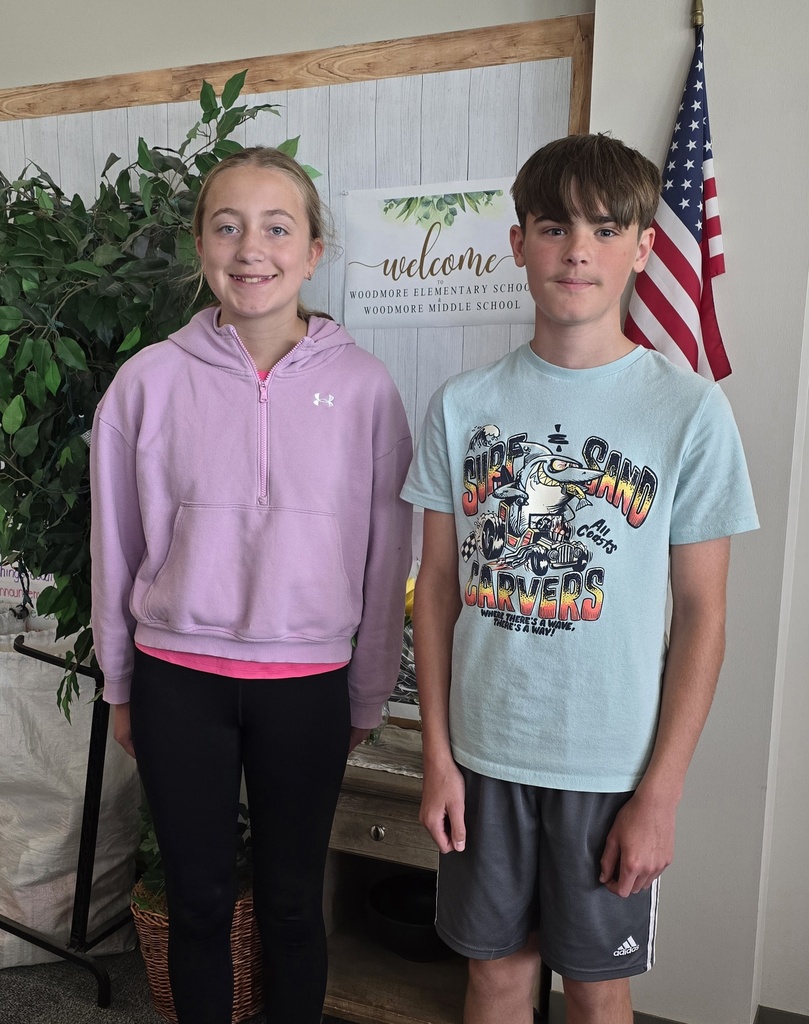 Emma and Dominic stand in front of the flag in the main office of the Middle School.