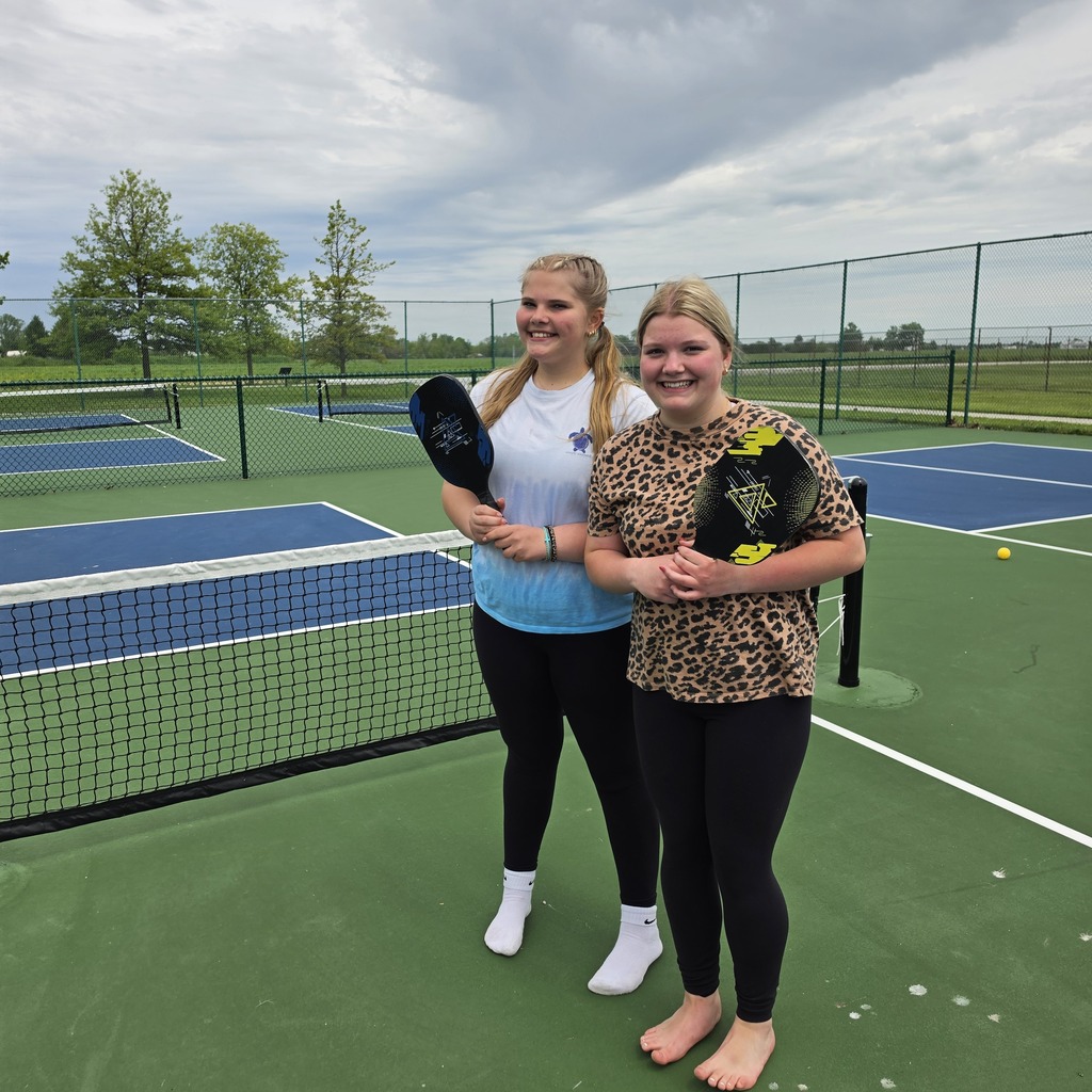 Two students pose on the pickleball courts with their paddles they used to play the game.