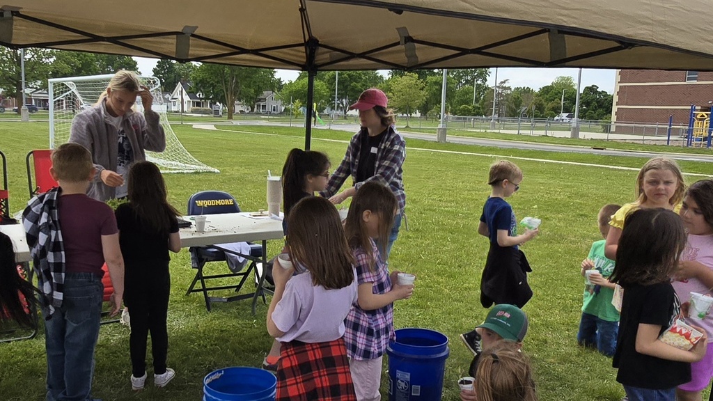 A group of students moves through a line to plant their own tomato plant to take home. Older students and a teacher help.