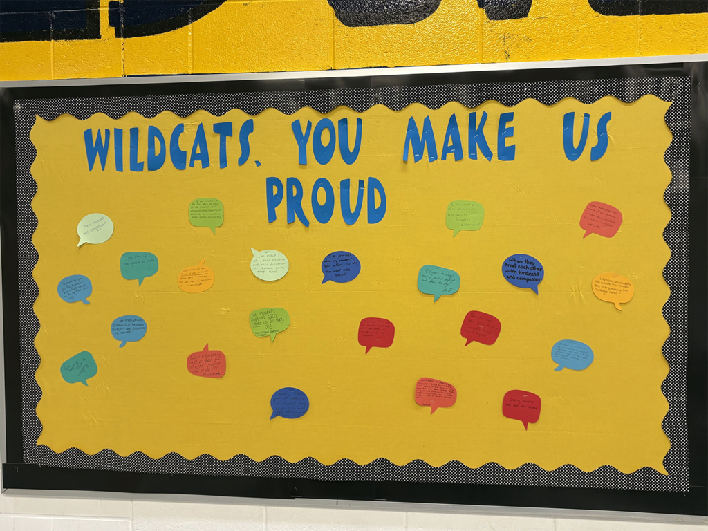 A yellow bulletin board with black and white checked border. The words "Wildcats, you make us proud" is in blue letters across the top. The teachers all wrote encouraging words on colorful thought bubbles and attached them to the board.