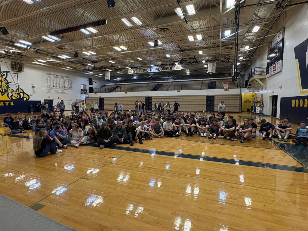 Students are gathered in the gym, sitting on the floor, waiting for Officer Psota to be duct taped to the wall.