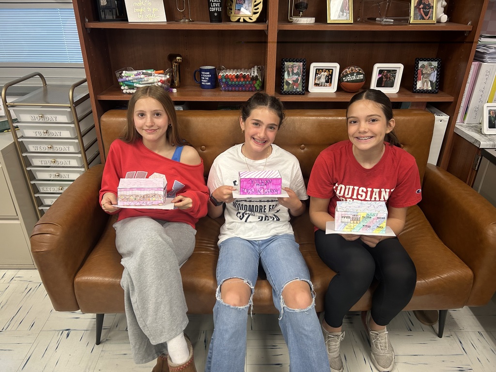Three students sit on a brown couch with their food trucks in their laps.
