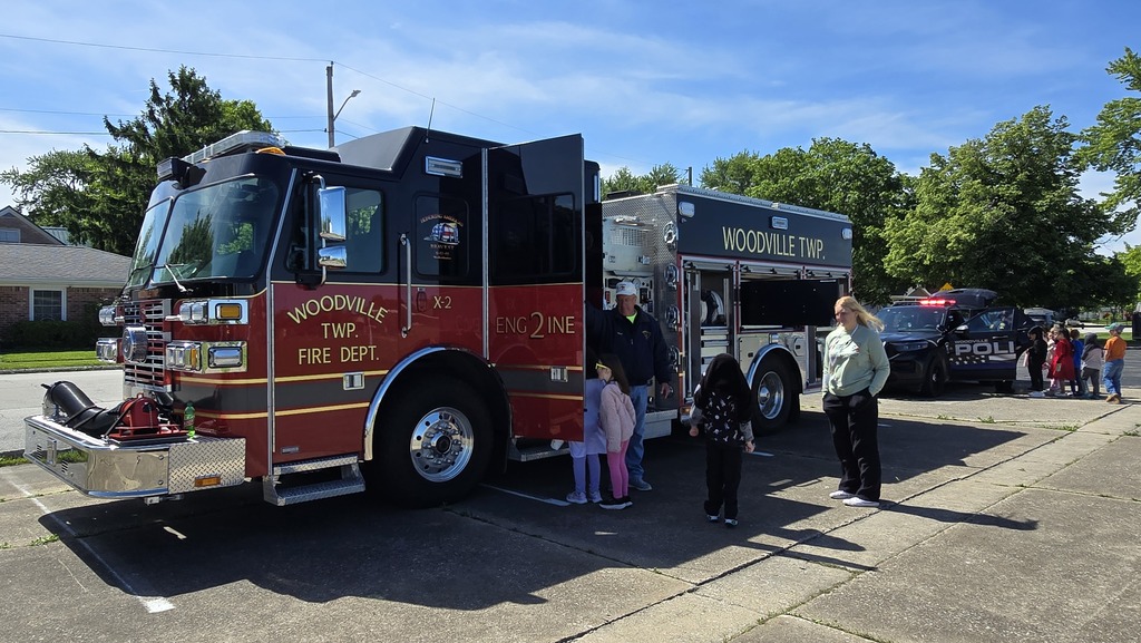 A Woodville fire truck is parked with students waiting to climb inside and check it out. A Woodville firefighter stands by the door, speaking with the waiting students.