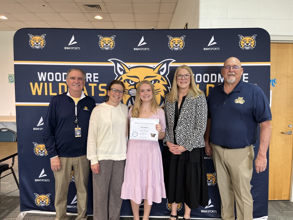 Zoey Bauder stands against the Woodmore backdrop with family and Woodmore representatives.