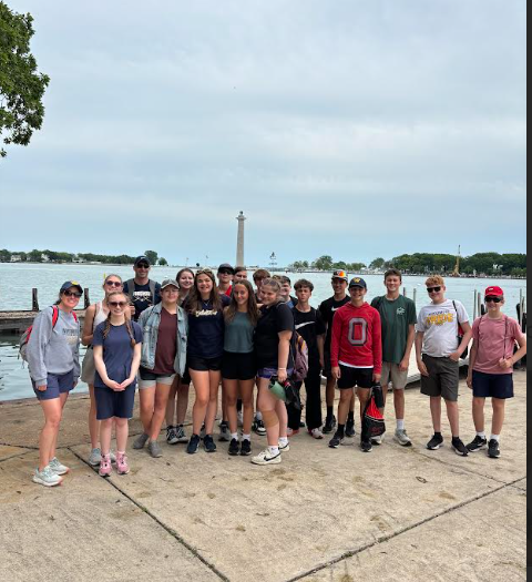 Students and teachers pose for a picture by the water with the Perry Monument in the background.