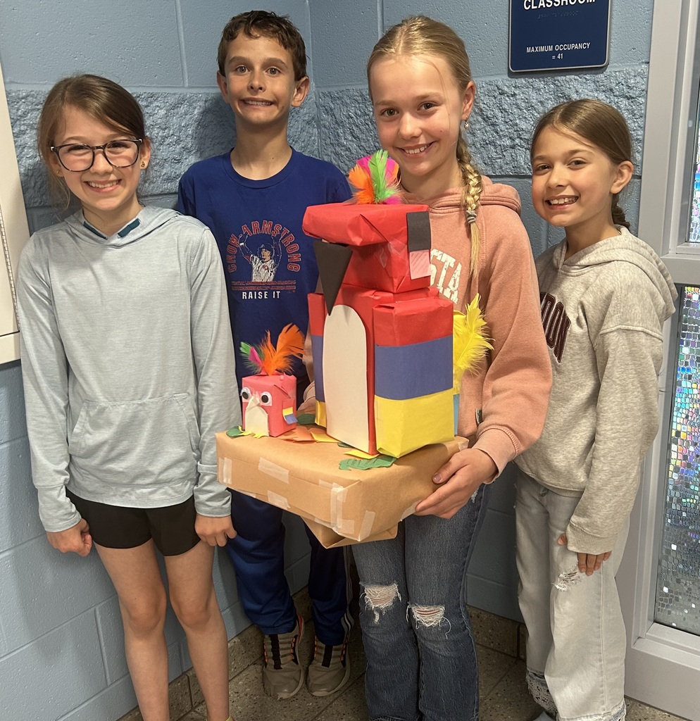 Four students hold their zoo shaped like a parrot in front of their classroom door.