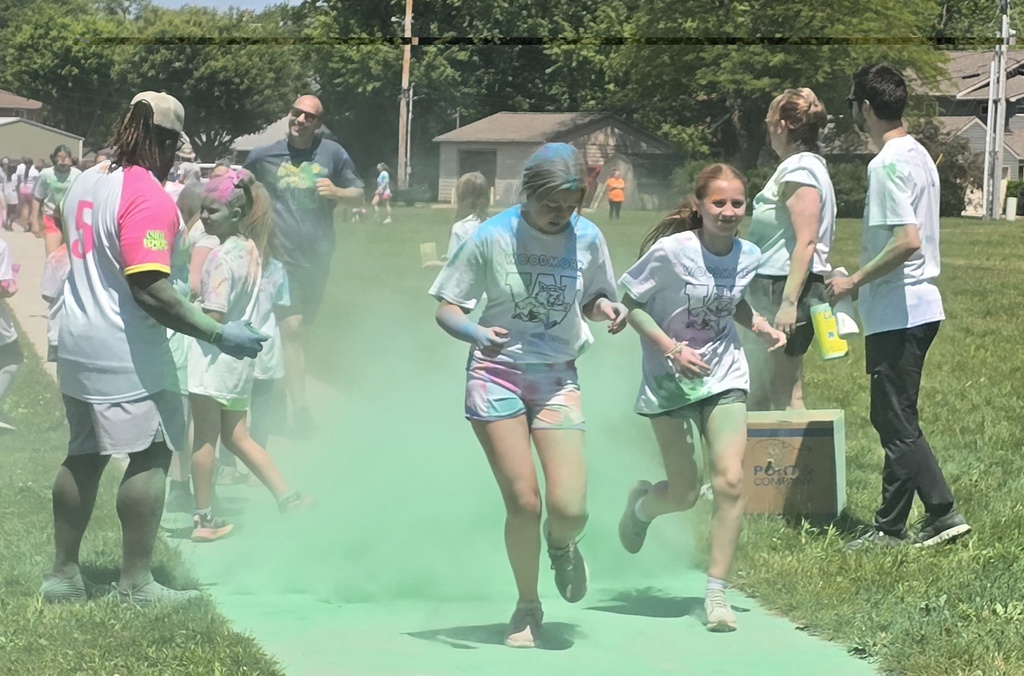 Students covered in colorful powder run through teachers tossing green powder.
