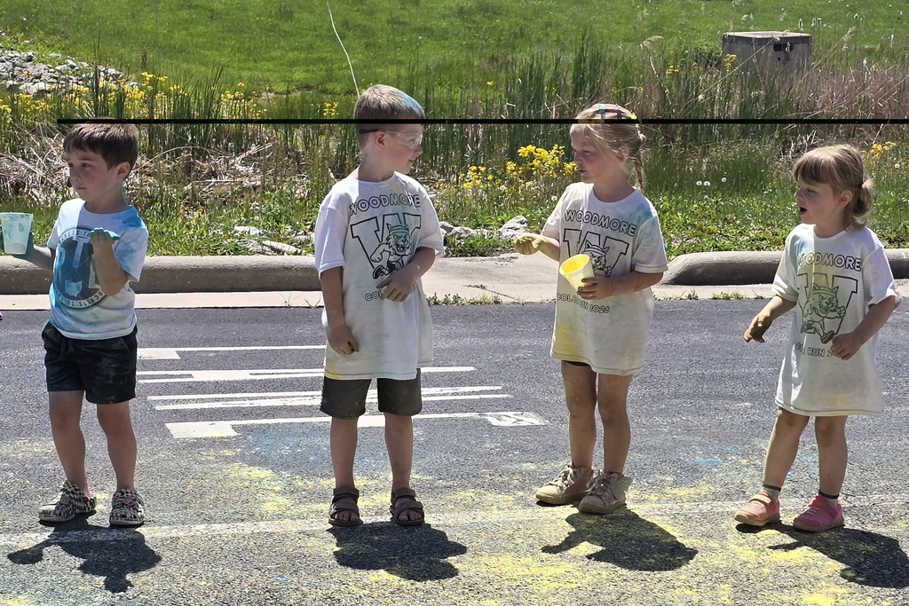 Four preschoolers wait with cups of yellow and blue powder for students to run past.