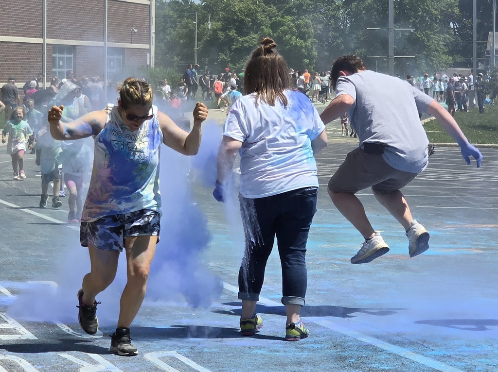 One teacher runs through a cloud of blue powder while another adult jumps up in the air to avoid the blue powder.