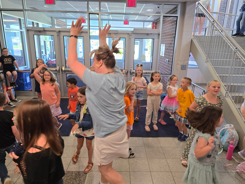 A teacher and elementary students stand in the front lobby, dancing to the last Dance Party of the year