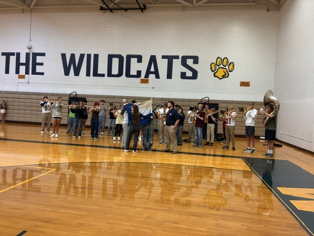 Marching band stands on the gym floor playing music for the pep rally.