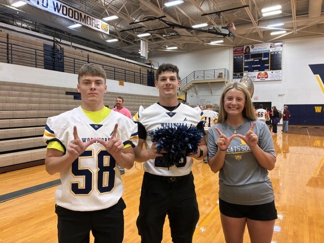 Three Woodmore students make a "W" with their hands in the gymnasium