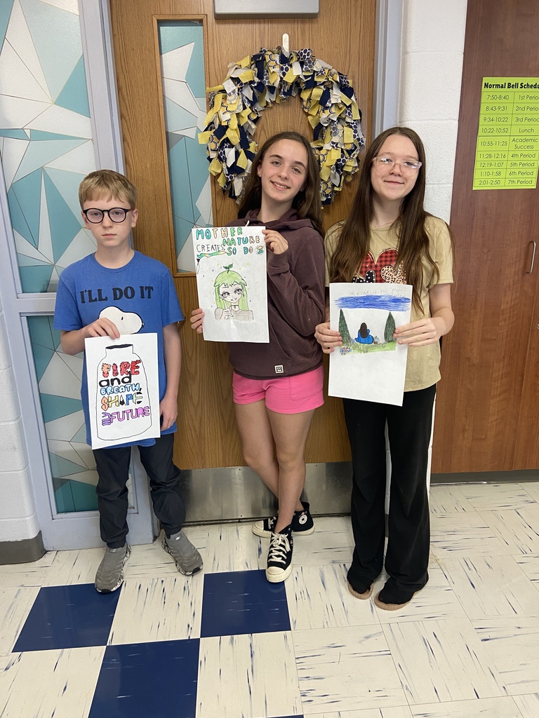 7th grade students hold their posters with their 6 word memoir illustrations in the classroom.