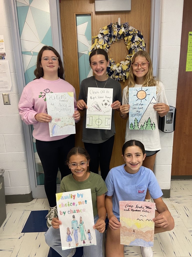 7th grade students hold their posters with their 6 word memoir illustrations in the classroom.